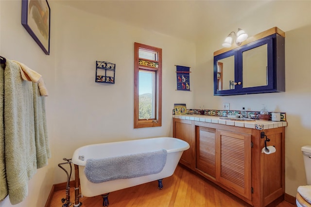 bathroom with baseboards, toilet, wood finished floors, a soaking tub, and vanity