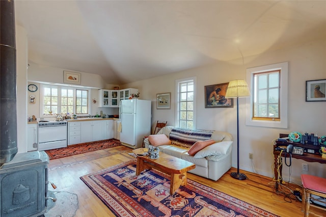 living area featuring a wood stove, light wood-style floors, and vaulted ceiling