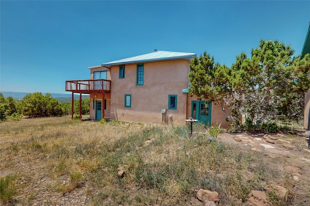 rear view of property featuring a deck, stucco siding, and metal roof