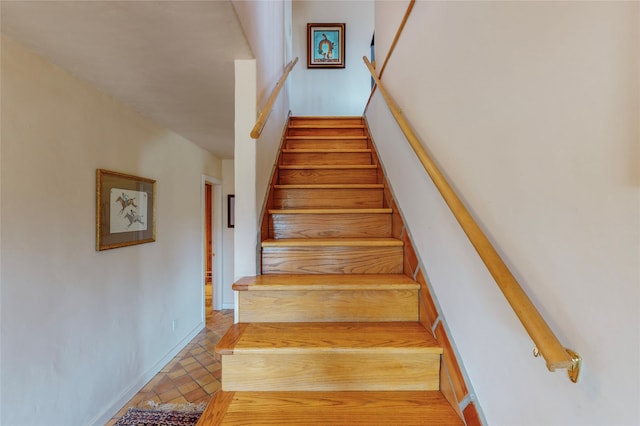 staircase featuring brick floor and baseboards