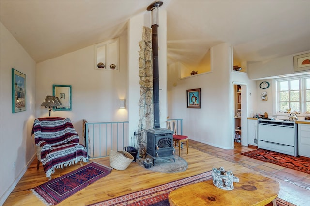 living room featuring light wood-style flooring, baseboards, a wood stove, and lofted ceiling