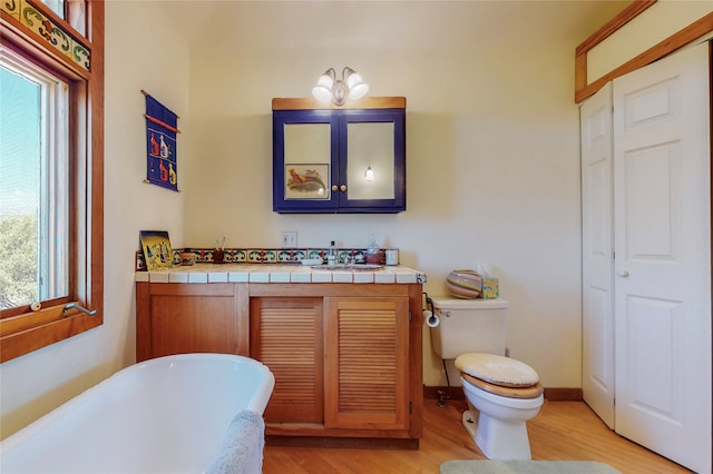 bathroom featuring baseboards, a freestanding bath, toilet, wood finished floors, and vanity