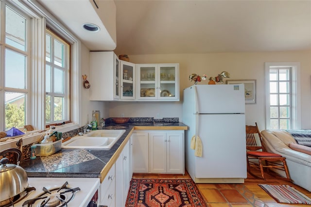 kitchen featuring freestanding refrigerator, a sink, glass insert cabinets, white cabinetry, and a wealth of natural light