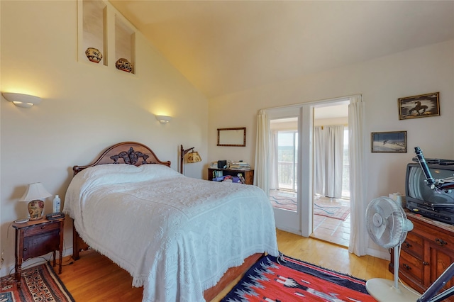 bedroom with access to exterior, lofted ceiling, and wood finished floors