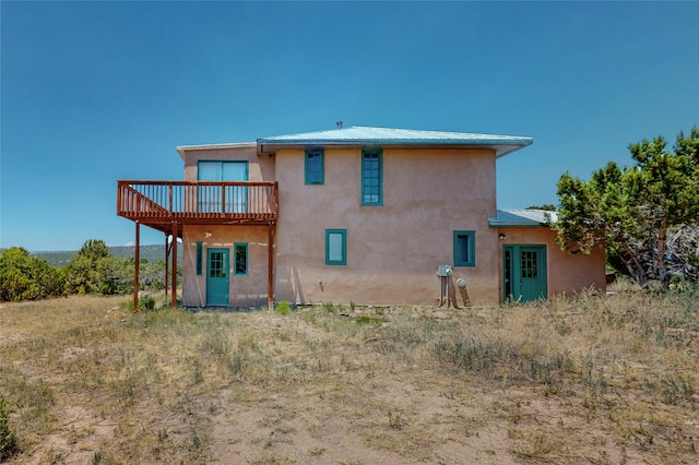 back of house featuring a wooden deck, stucco siding, and metal roof