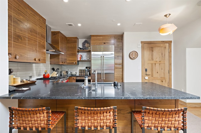 kitchen with wall chimney range hood, tasteful backsplash, stainless steel appliances, and a kitchen bar