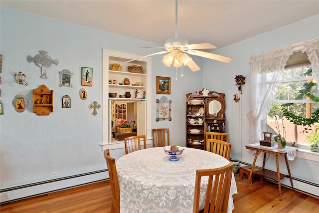 dining space featuring built in shelves, ceiling fan, a baseboard radiator, and light hardwood / wood-style floors