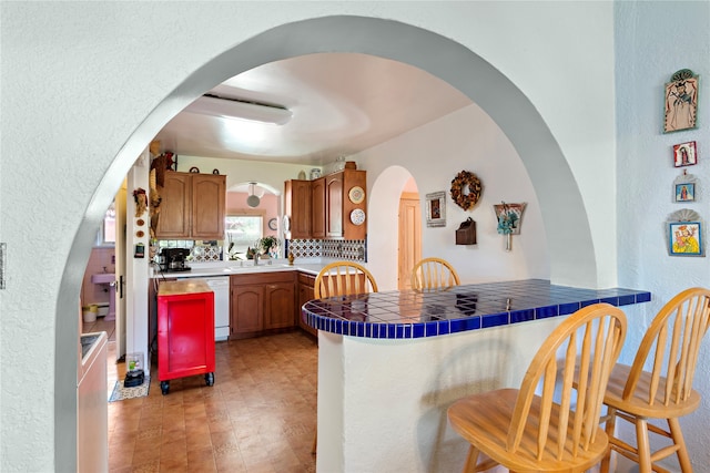 kitchen with tile countertops, dishwasher, kitchen peninsula, and tasteful backsplash