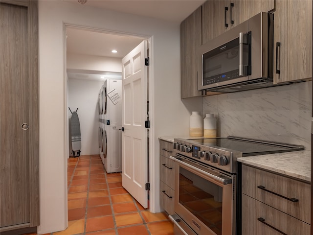 kitchen featuring appliances with stainless steel finishes, light stone counters, light tile floors, washer / clothes dryer, and backsplash