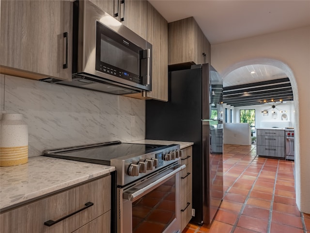 kitchen featuring light stone countertops, stainless steel appliances, tasteful backsplash, and light tile floors