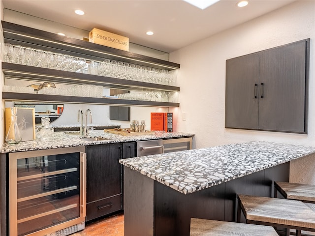 bar featuring beverage cooler, light stone countertops, and sink