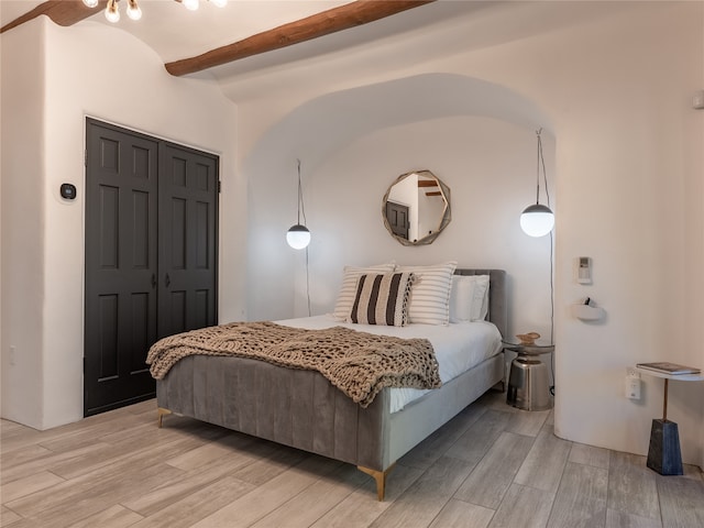 bedroom with a closet, light wood-type flooring, and beamed ceiling