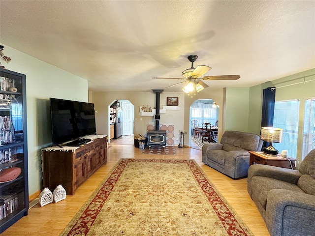 living room with ceiling fan, light hardwood / wood-style flooring, a wealth of natural light, and a wood stove