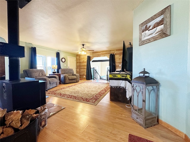 living room with light hardwood / wood-style flooring, a textured ceiling, wooden walls, a wood stove, and ceiling fan