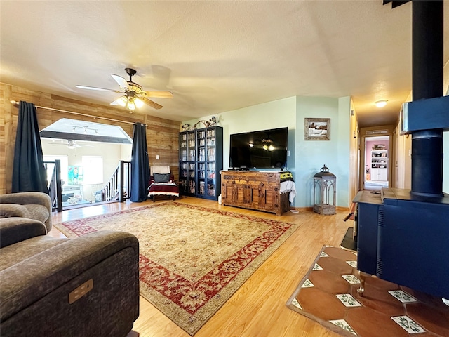 living room with wood walls, light hardwood / wood-style flooring, a wood stove, and ceiling fan