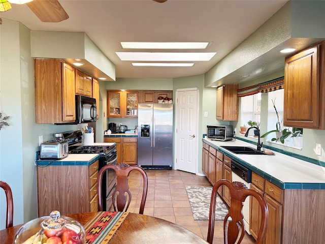 kitchen featuring ceiling fan, gas range, stainless steel fridge, light tile patterned flooring, and a skylight