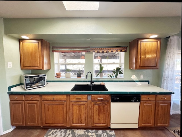 kitchen with dark hardwood / wood-style flooring, tile counters, a skylight, white dishwasher, and sink