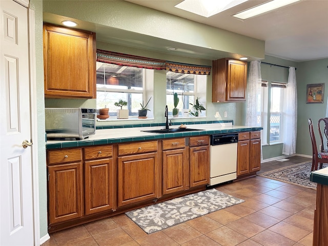 kitchen with dishwasher, light tile patterned flooring, a skylight, sink, and tile countertops