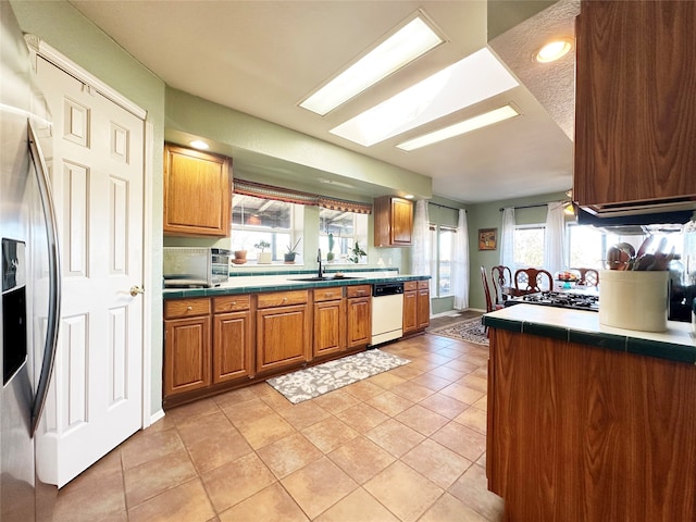 kitchen featuring dishwasher, a skylight, stainless steel fridge, light tile patterned floors, and sink