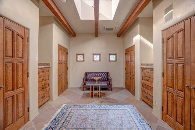 living area with a skylight, beam ceiling, and light tile flooring