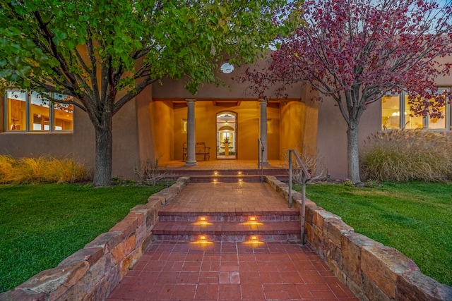 exterior entry at dusk with a lawn and a patio area