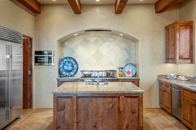 kitchen with a center island with sink, appliances with stainless steel finishes, light stone counters, and sink