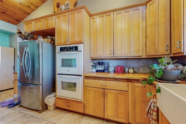 kitchen with white double oven, light tile flooring, stainless steel fridge, vaulted ceiling, and wooden ceiling