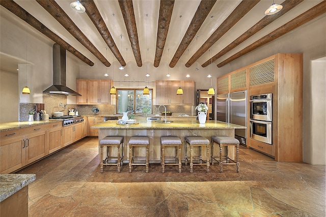 kitchen featuring hanging light fixtures, decorative backsplash, a center island with sink, and wall chimney exhaust hood