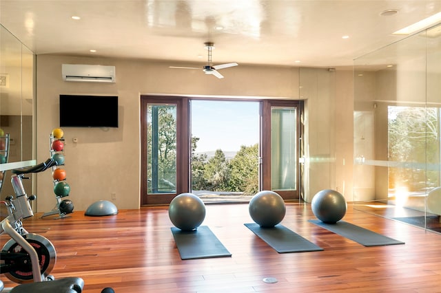 exercise room featuring ceiling fan, hardwood / wood-style flooring, a wall mounted AC, and plenty of natural light