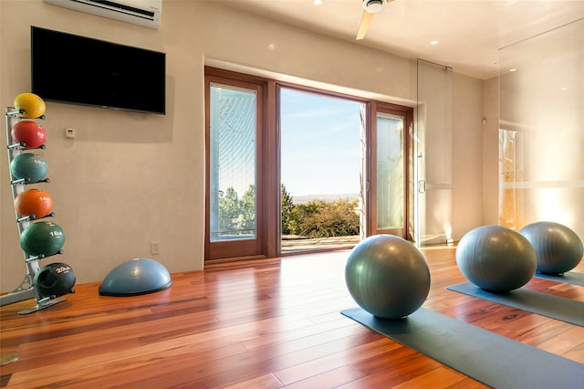 exercise area with an AC wall unit, wood-type flooring, and a healthy amount of sunlight