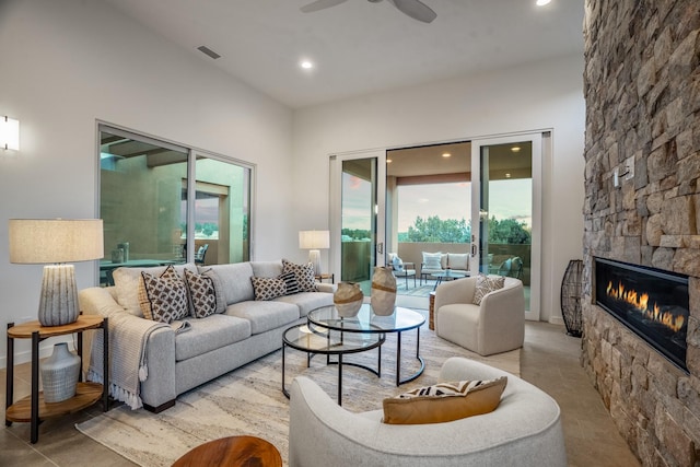 living room with ceiling fan, a stone fireplace, and a wealth of natural light