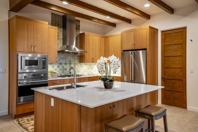 kitchen with stainless steel appliances, an island with sink, wall chimney range hood, decorative backsplash, and a kitchen breakfast bar