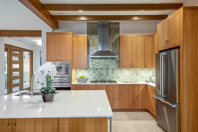 kitchen featuring stainless steel appliances, wall chimney exhaust hood, decorative backsplash, a kitchen island with sink, and beam ceiling