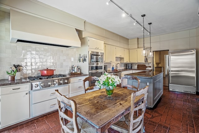 kitchen featuring tasteful backsplash, a kitchen island, premium range hood, dark stone countertops, and built in appliances