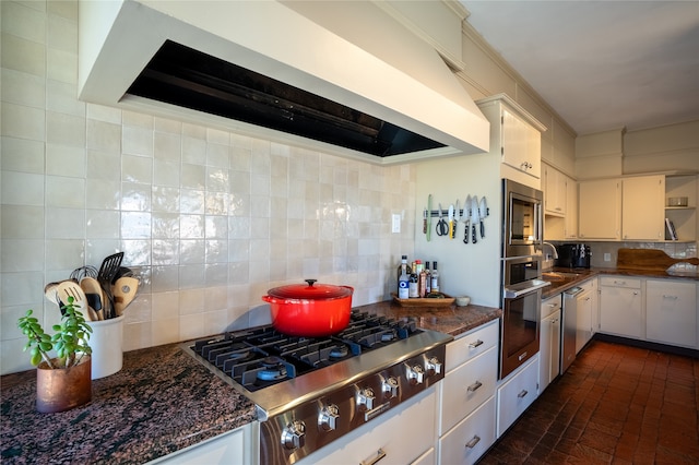 kitchen with custom range hood, dark stone counters, backsplash, stainless steel appliances, and white cabinetry