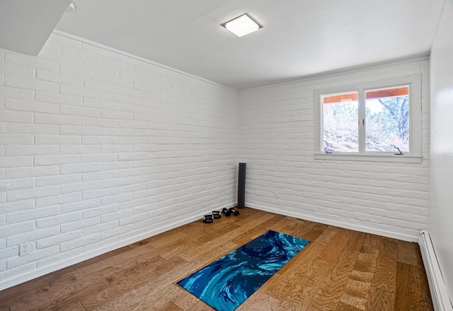 exercise area featuring a baseboard radiator, brick wall, and hardwood / wood-style flooring