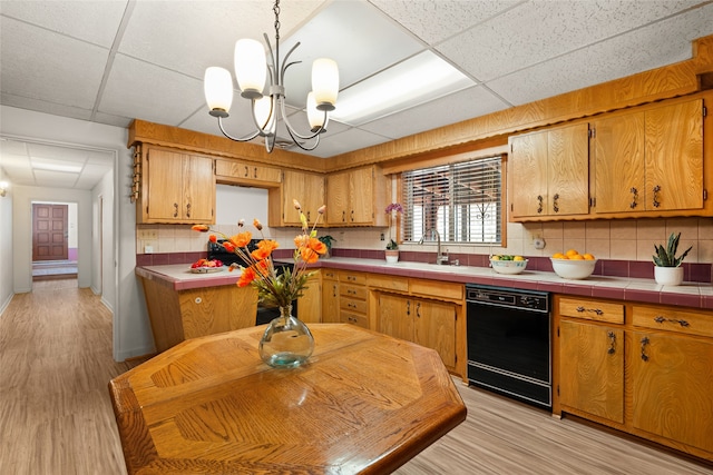 kitchen featuring an inviting chandelier, a drop ceiling, light wood-type flooring, backsplash, and black dishwasher