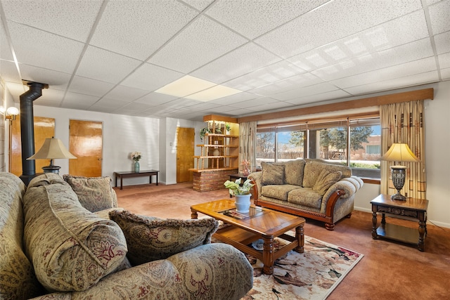 carpeted living room featuring a wood stove and a drop ceiling