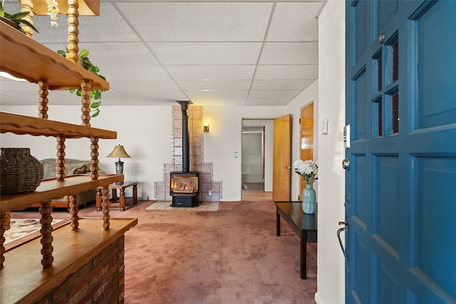 interior space with a wood stove, a paneled ceiling, and light carpet