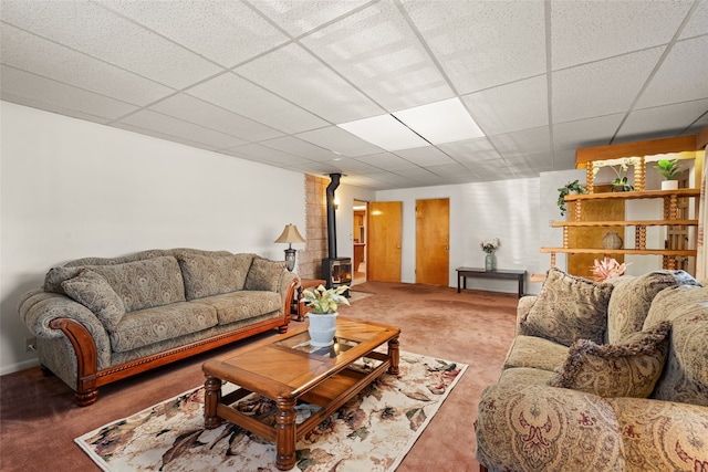 living room featuring a paneled ceiling, dark colored carpet, and a wood stove