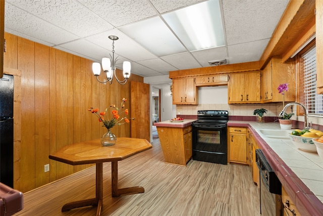 kitchen with wooden walls, light hardwood / wood-style floors, sink, a chandelier, and black appliances