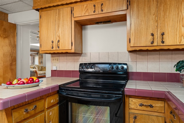 kitchen featuring backsplash, a paneled ceiling, tile countertops, and black / electric stove