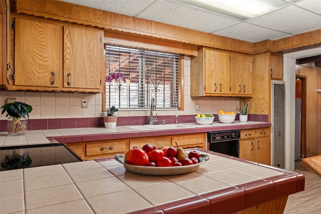 kitchen featuring a drop ceiling, tasteful backsplash, sink, tile counters, and black dishwasher