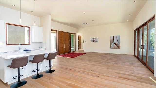 interior space featuring a breakfast bar, white cabinets, light wood-type flooring, pendant lighting, and sink