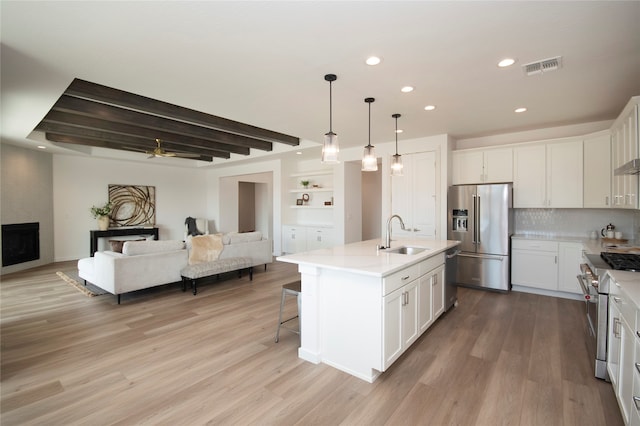 kitchen featuring high quality appliances, an island with sink, a fireplace, ceiling fan, and hanging light fixtures