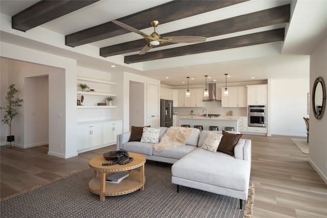 living room featuring ceiling fan, sink, beamed ceiling, and light hardwood / wood-style floors