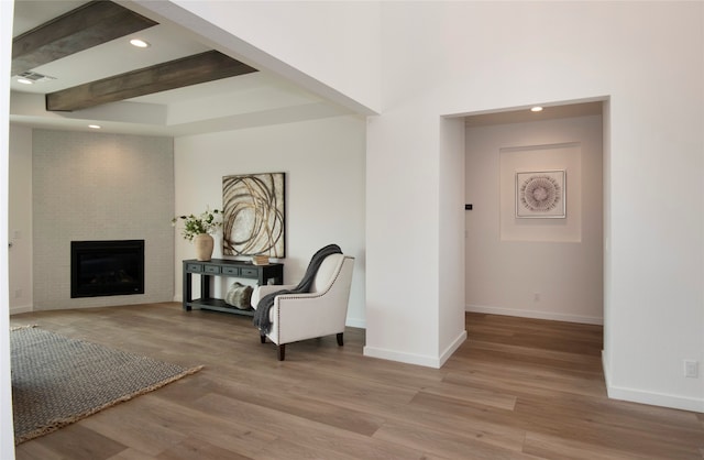 sitting room featuring light hardwood / wood-style floors, a fireplace, a tray ceiling, and beamed ceiling