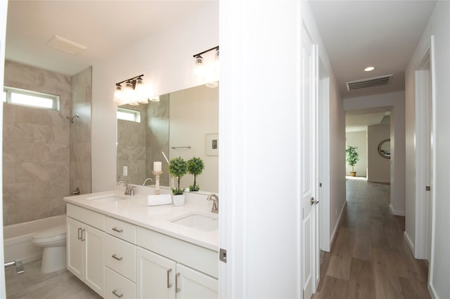 full bathroom featuring dual vanity, wood-type flooring, toilet, and tiled shower / bath