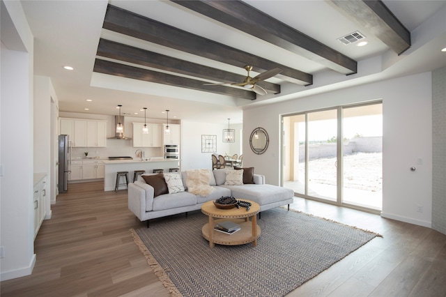 living room featuring sink, wood-type flooring, ceiling fan, and beamed ceiling