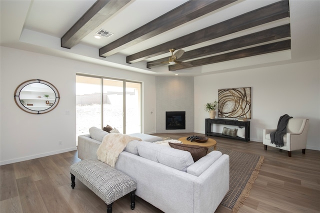 living room featuring dark wood-type flooring, beam ceiling, ceiling fan, and a fireplace